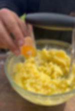 one egg yolk being added to the bowl of mashed potatoes