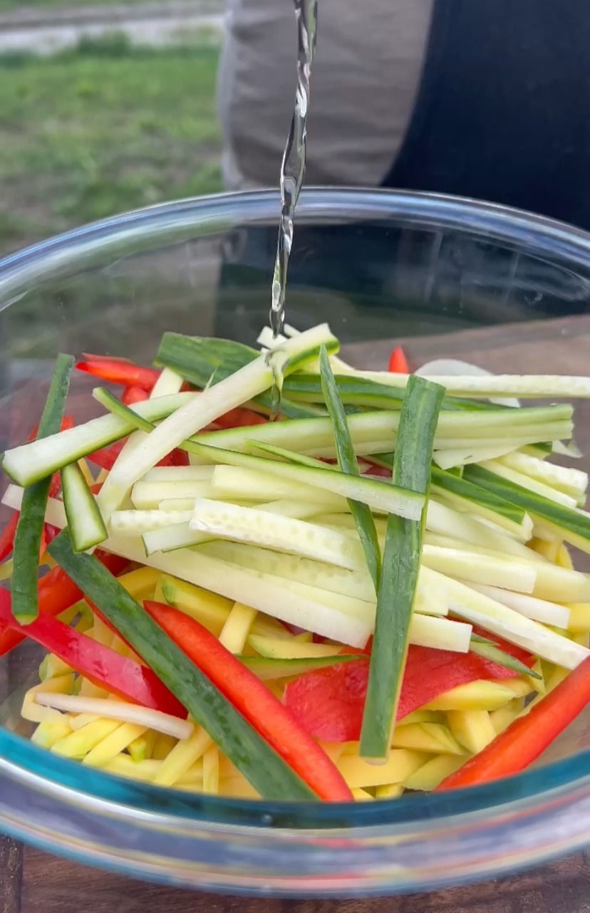 seasoned rice wine vinegar being poured into a bowl with sliced mango, red pepper and slice cucumber