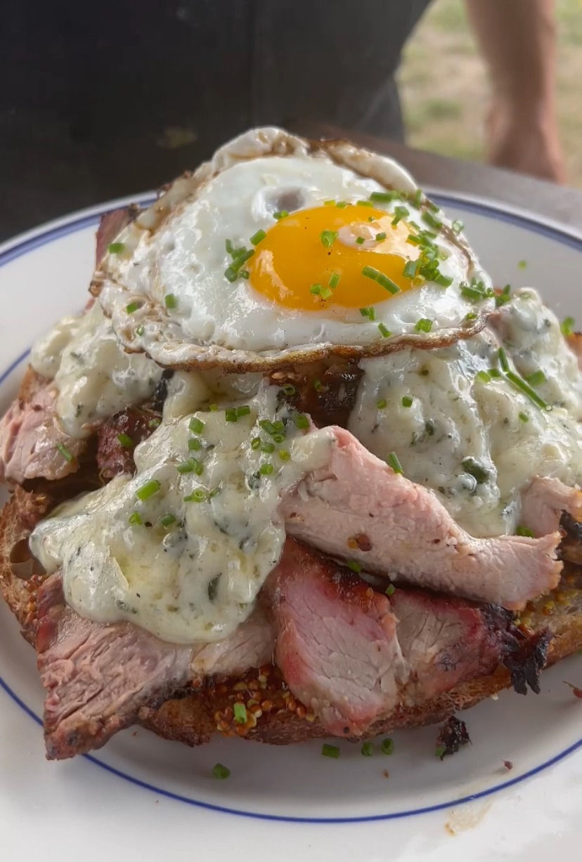 smoked pork loin croque madame with a sunny side up egg on top and chopped chives to garnish