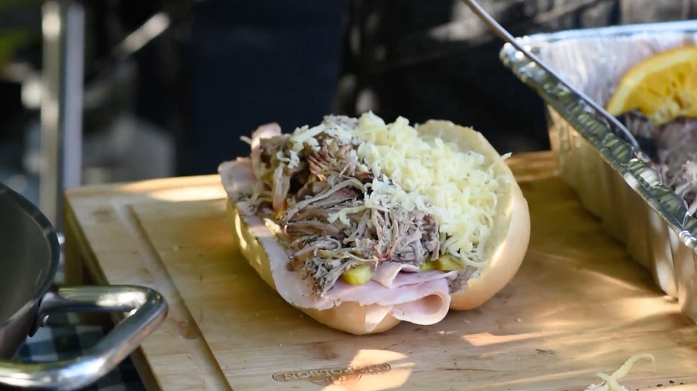 building a Cubano sandwich with ham, pulled pork, mustard, pickles and grated Swiss cheese