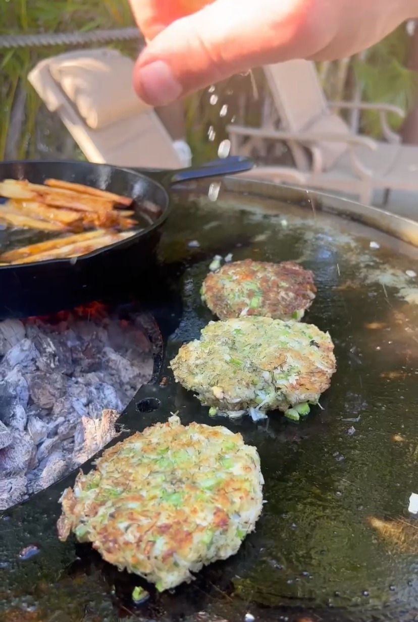 lemon juice being squeezed over the crab cakes cooking on the plancha