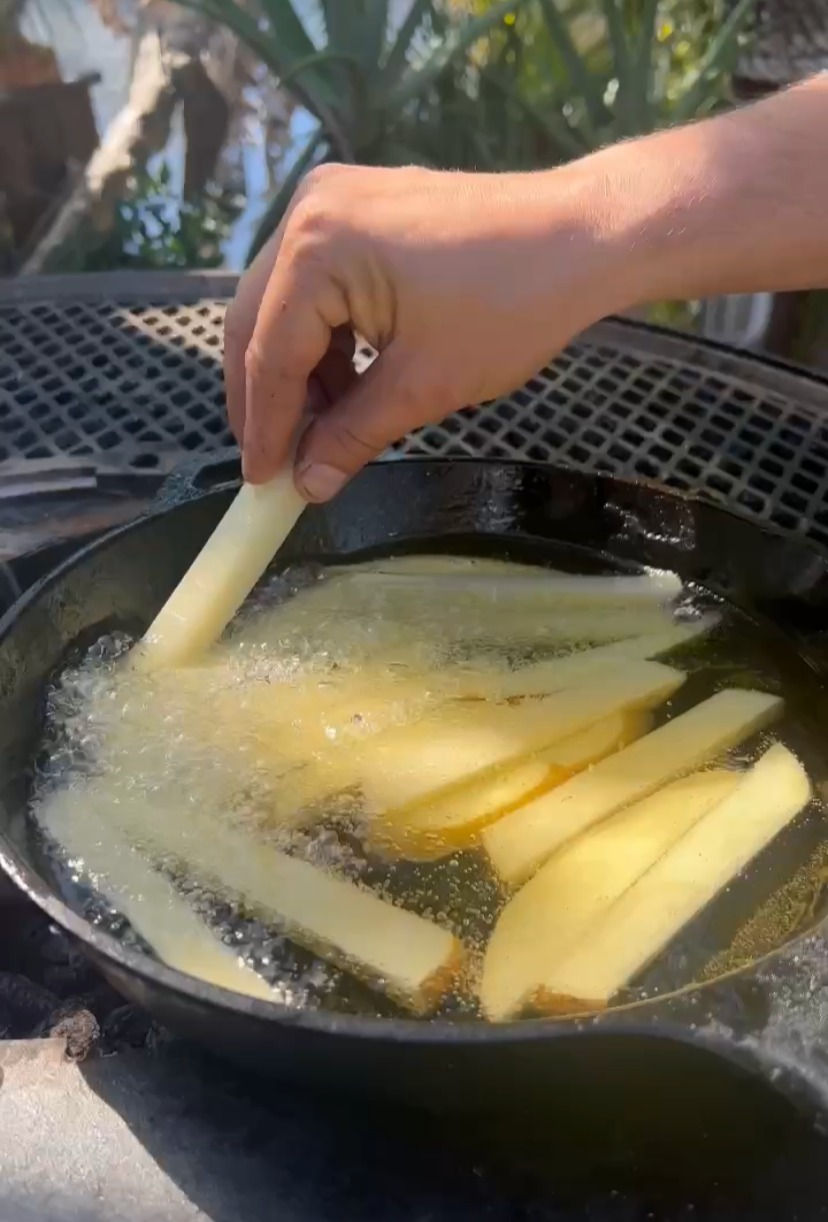 thick-cut fries frying in oil in a cast iron pan on the plancha