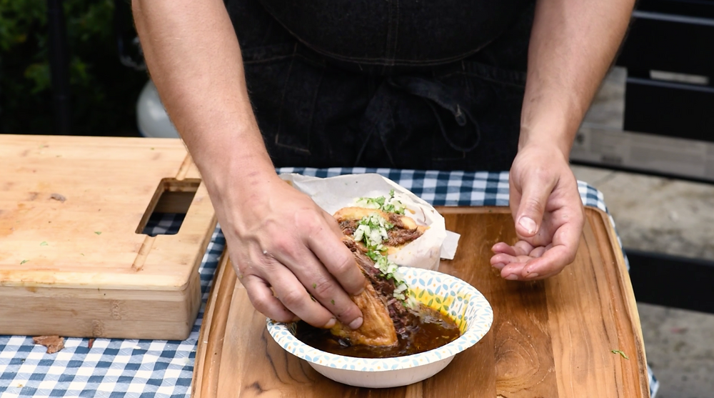 the birria beef torta being dipped into a bowl of broth