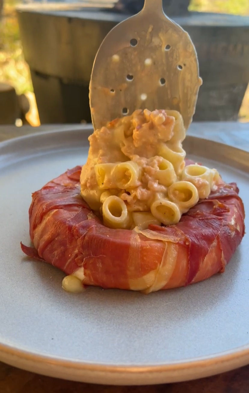 lobster mac and cheese being spooned into the centre of the smoked prosciutto-wrapped brie