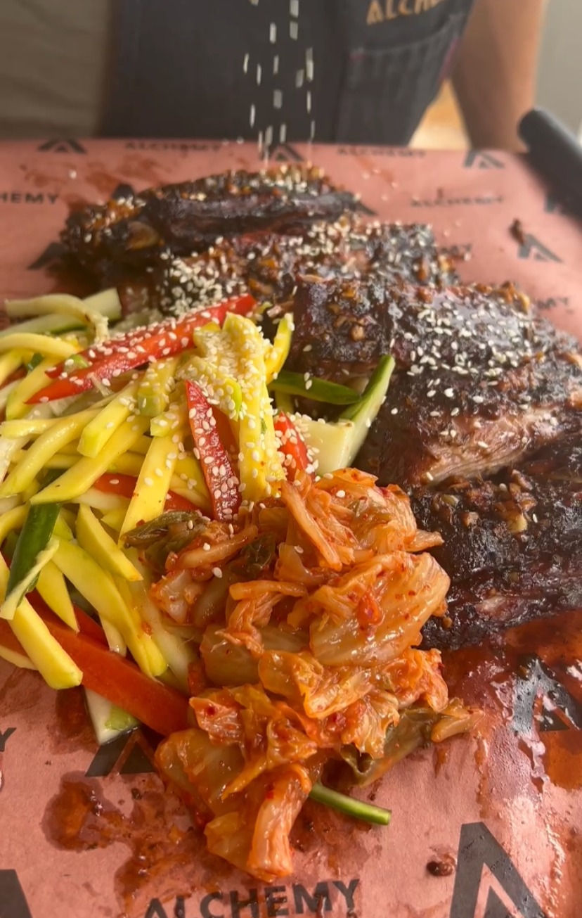 smoked pork side ribs being garnished with sesame seeds and served with mango slaw and kimchi