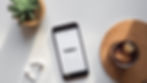 A smart phone lies on a white table next to a plant with the message "Hello!"
