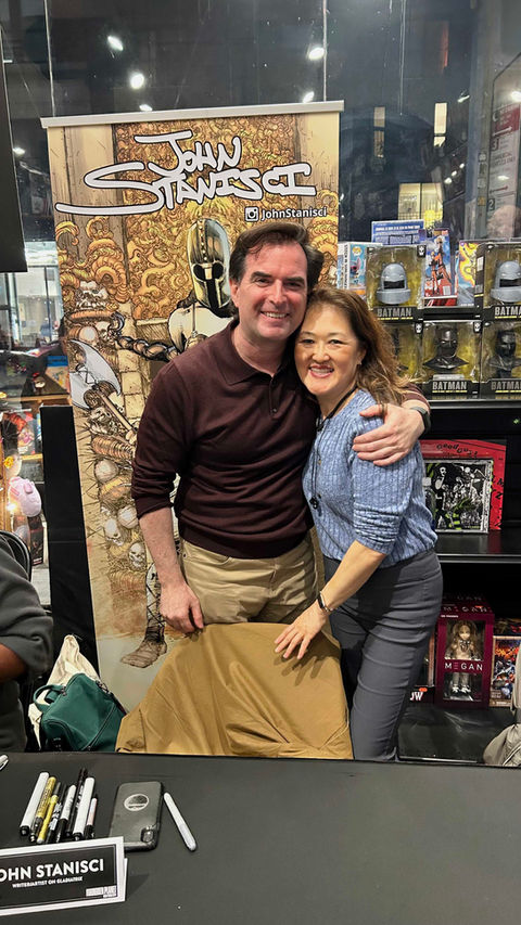 John Stanisci puts his arm around his wife Suzie Cho in a blue sweater at Forbidden Planet NYC, mood is celebratory