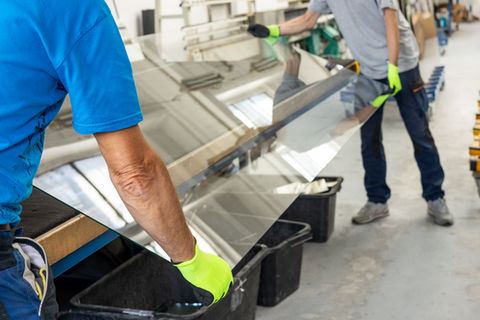 Workers handling large glass sheets in a factory, safety first, hard at work.