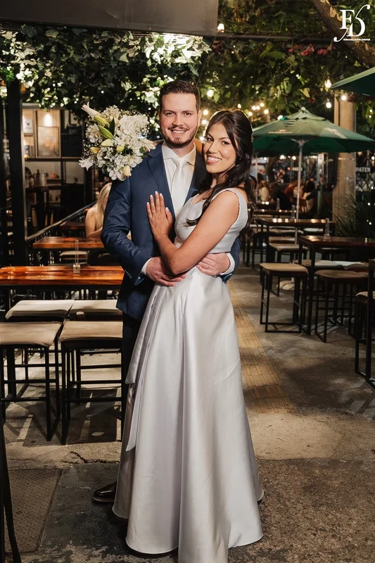 Casal Rafaella e Rafael sorrindo com buquê de lírios brancos após cerimônia de casamento