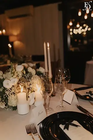 Mesa das noivas com arranjo orgânico branco, velas e bolo de casamento ao fundo no Le Bistrot Gourmet
