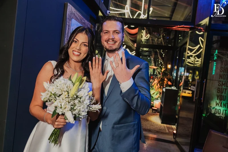 Casal Rafaella e Rafael sorrindo com buquê de lírios brancos após cerimônia de casamento