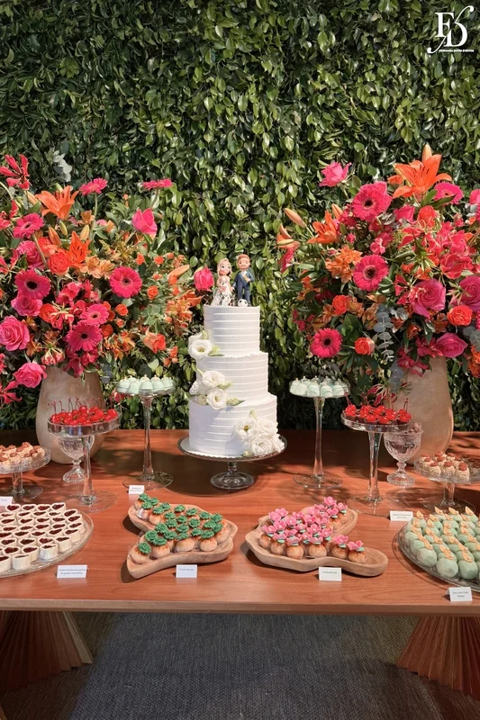 Mesa de doces de casamento com decoração de flores coloridas laranja e rosa e muro inglês