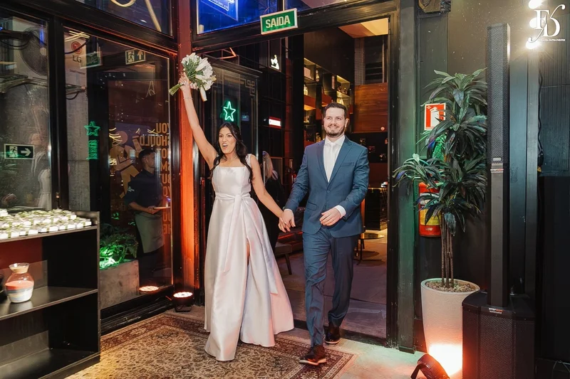 Casal Rafaella e Rafael sorrindo com buquê de lírios brancos após cerimônia de casamento
