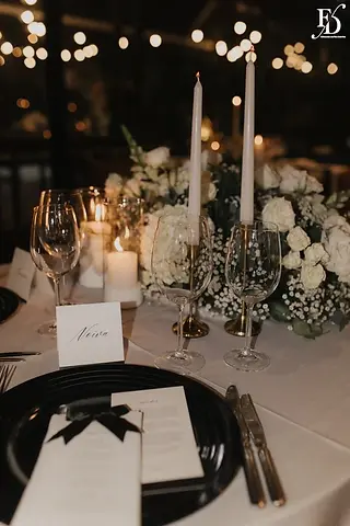 Mesa das noivas com arranjo orgânico branco, velas e bolo de casamento ao fundo no Le Bistrot Gourmet