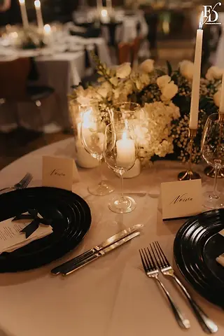 Mesa das noivas com arranjo orgânico branco, velas e bolo de casamento ao fundo no Le Bistrot Gourmet
