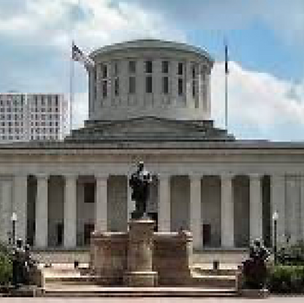 Historic capitol building with columns, dome, and statues. Flags waving, blue sky. Grand, solemn atmosphere.