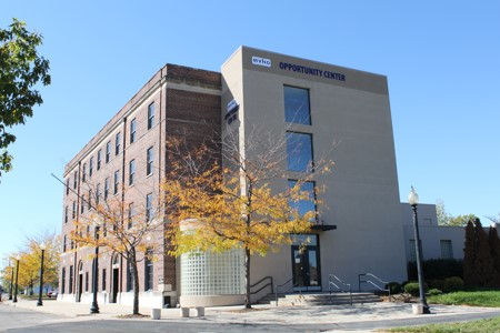 Modern brick-and-beige building labeled Opportunity Center on a sunny street, with autumn trees and clear blue sky.