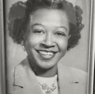 Framed black-and-white portrait of a smiling woman with curled hair and a light jacket, with a small signature at bottom right.