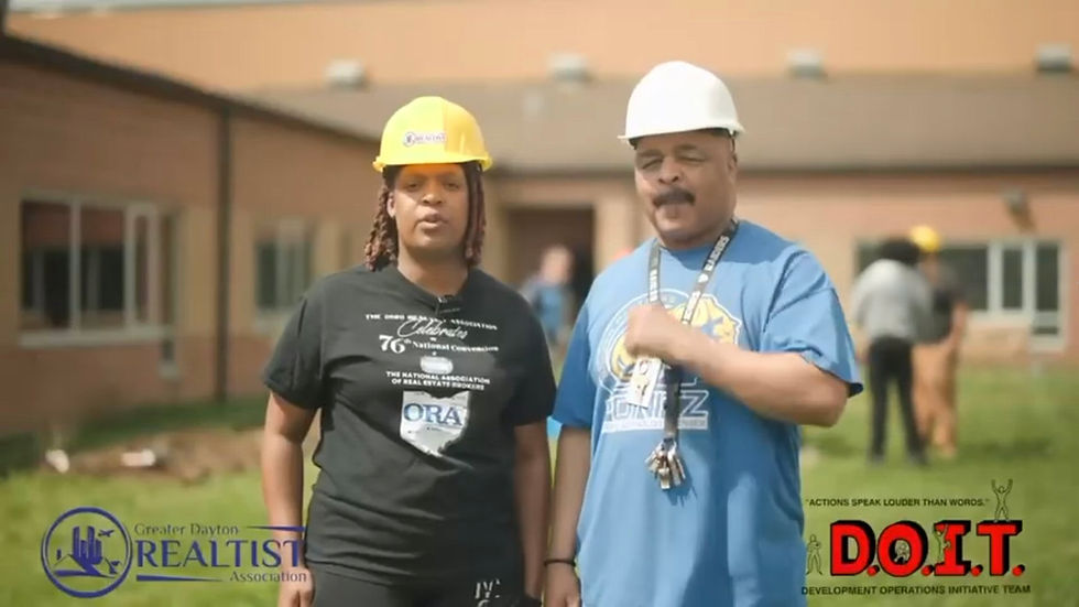 Two people in hard hats stand outside a brick building, with event logos and D.O.I.T. text overlaid, looking serious.