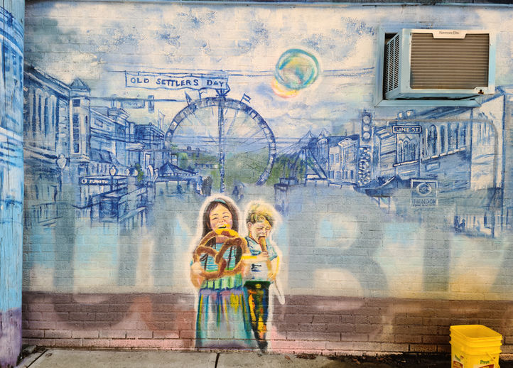 Columbia City Old Settlers, Children eating fun fair food in the foreground in bright vibrant colors. Ghosted behind them and against the cityscape in large words Columbia City.