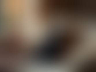 Black cat with yellow eyes sitting on a beige couch in a cozy living room with a lamp and blanket.