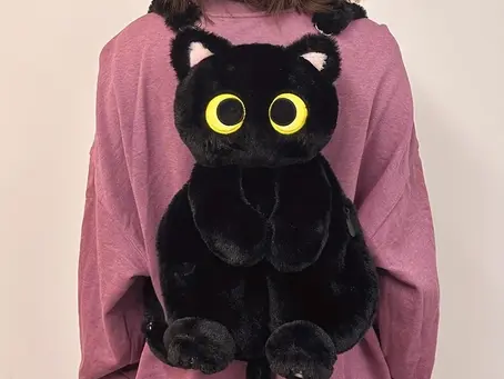 A black cat plush backpack resting on the back of a girl wearing a pink shirt