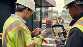 Two men on a construction site entry point completing work readiness inputs on a tablet and phone.