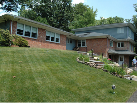 Brick ranch-style home with a sloped lawn, stone-edged garden steps, and a gray addition, designed by Robert Algarin Architect.
