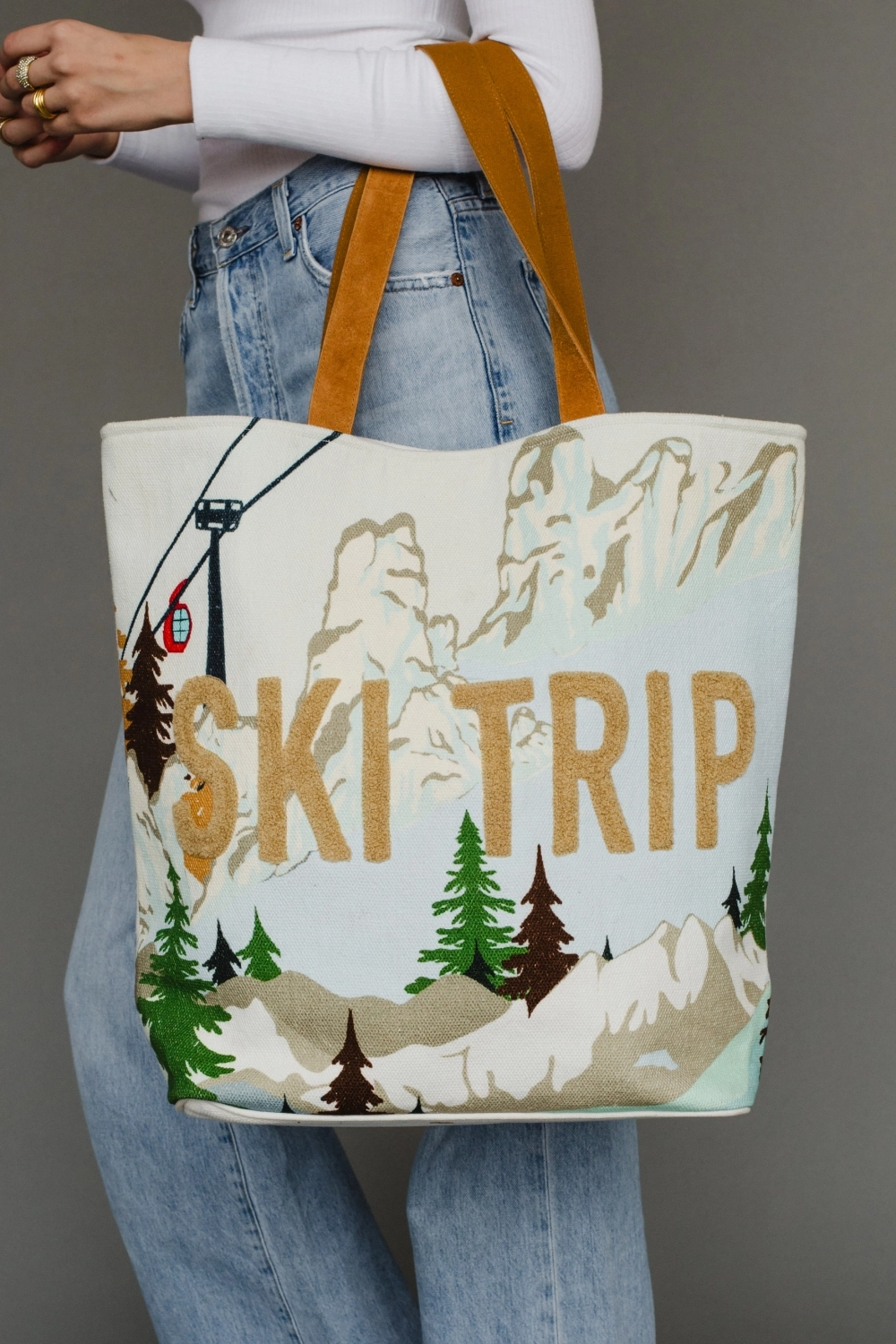 White, Light Blue & Green Ski Resort Scene Tote from the front being held by leather straps.