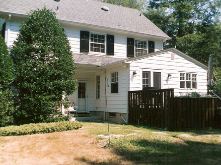 Two-story white home with an attached addition, fenced backyard, and surrounding greenery.