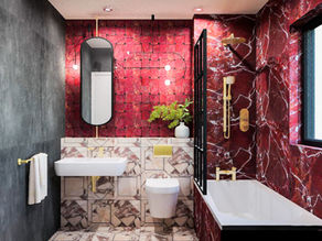 Luxurious bathroom with red marble walls, a white sink, and a bathtub. Gold fixtures, a large mirror, and greenery add elegance.