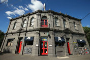 Front of the Palace Hotel. Solid stone building, red doors, blue sky.