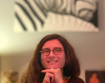 mon portrait : brune aux cheveux longs bouclés. Sourire. Port de lunettes rondes en écaille. Mains sous le menton.
