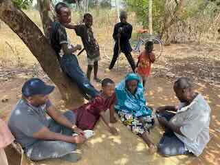 A family gathers under a tree with Kulea Villages staff during a home visit outside Dar es Salaam. 