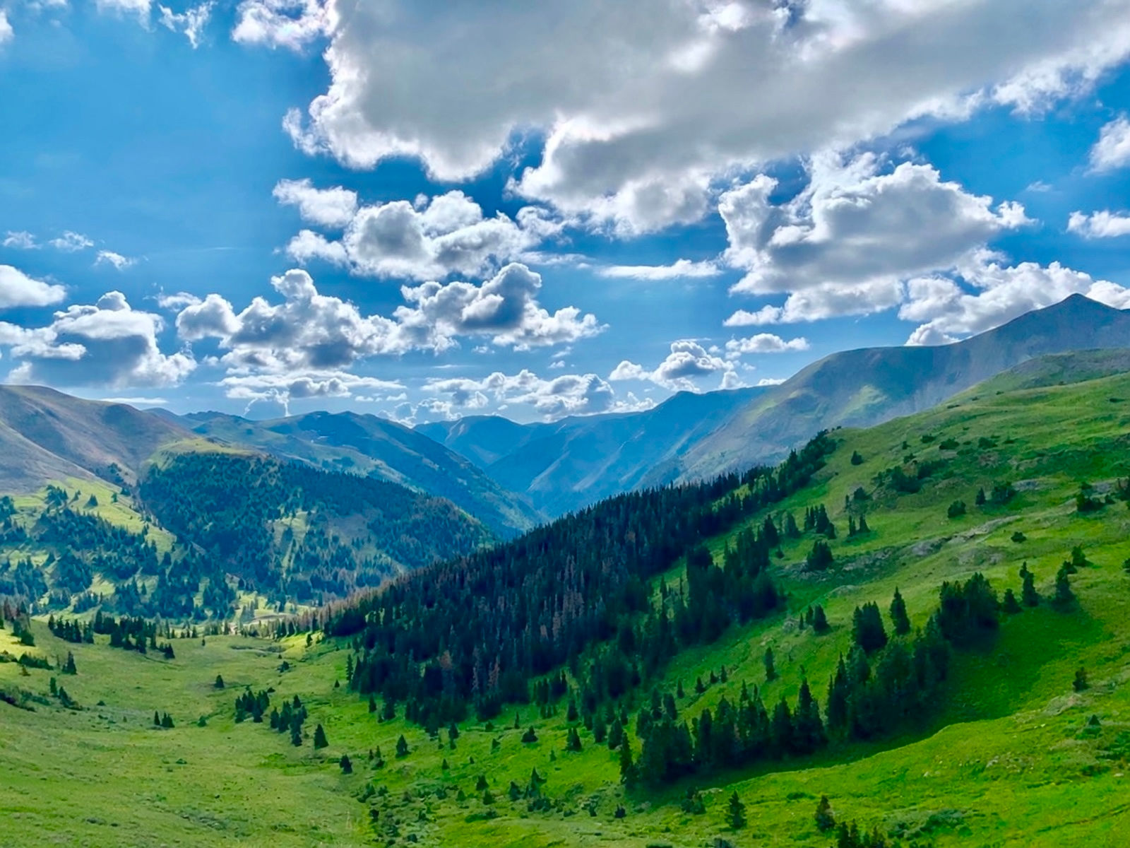 What the Rain Brings - monsoon clouds gathering over a green mountain valley with bright open land below