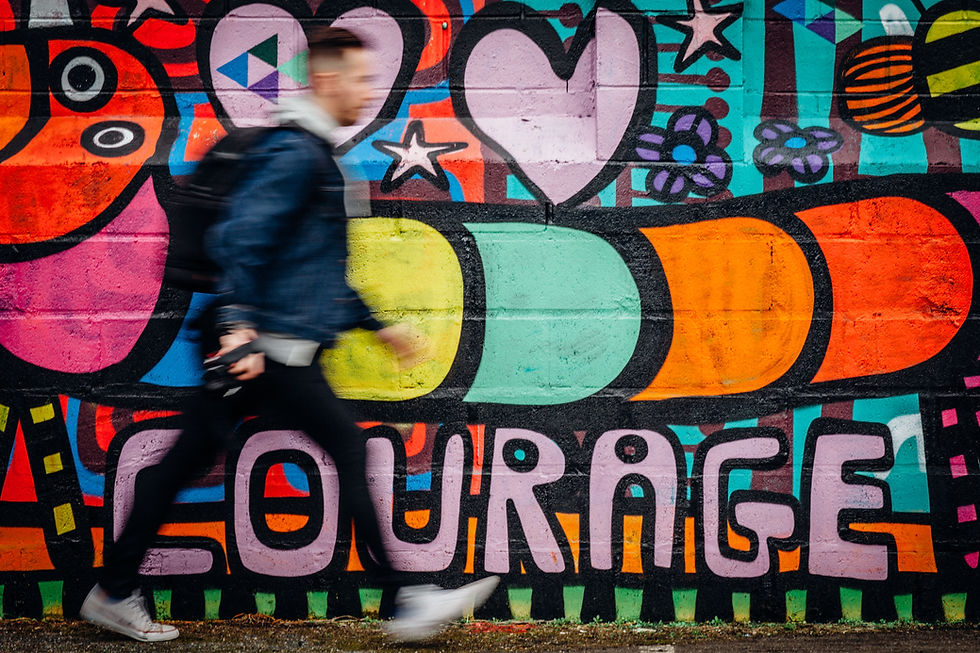 A man walks rapidly in front of a brightly colored mural with a cartoon caterpillar, that says the word "Courage."