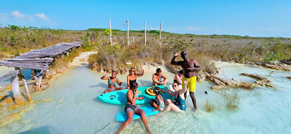 une famille dans l'eau turquoise qui mange des fruits sur un paddle à bacalar
