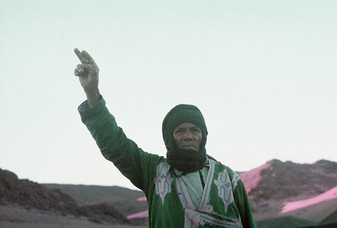 Man in green jacket raising finger, Moroccan desert landscape
Alt: Portrait man green jacket Moroccan desert Morocco — travel documentary photographer Andie Szatmari