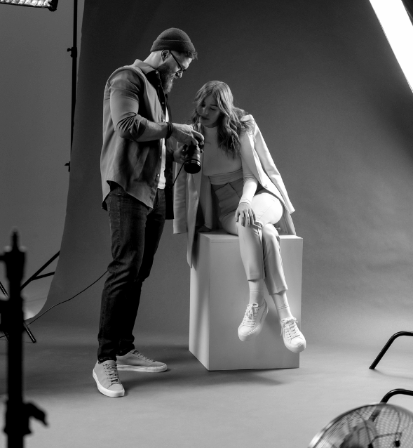 Black and white photo of a professional studio photoshoot. A photographer shows a photo preview on his camera to a female.
