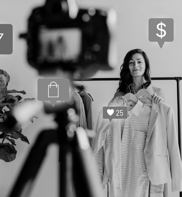 Black and white image of a woman livestreaming or recording a fashion video in front of a camera on a tripod.