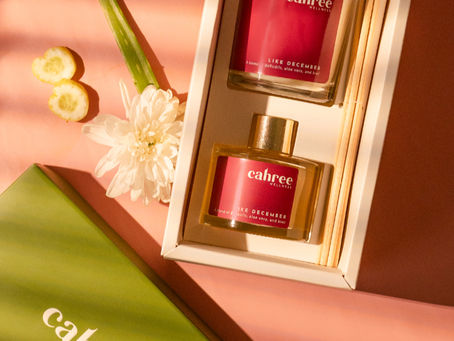 Cahree Wellness gift box with Like December reed diffuser and candle on a peach background with floral accents