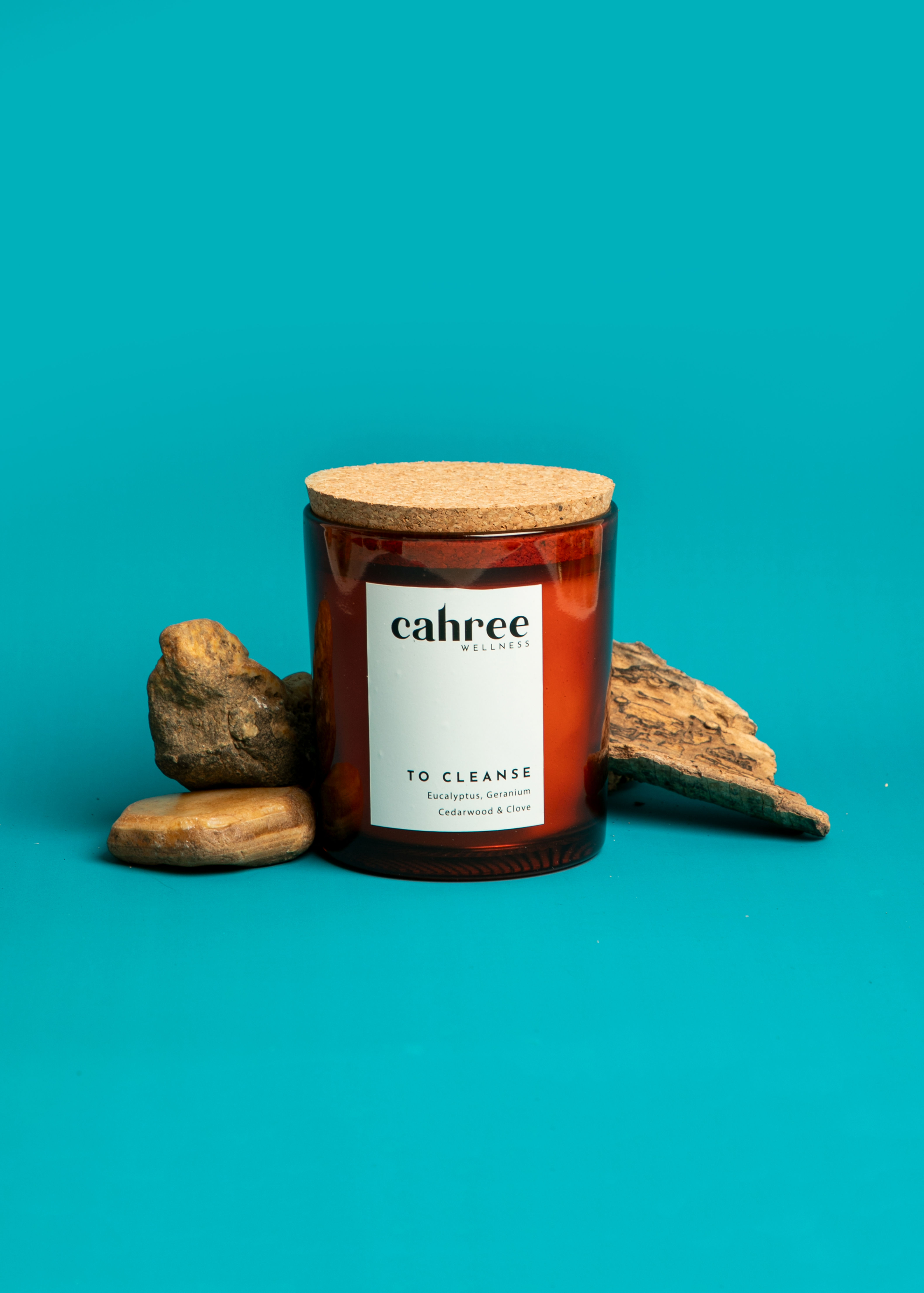 "Cahree To Cleanse aromatherapy soy candle with cork lid, styled with stones and bark on a clean blue background