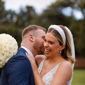 Bride laughing as groom kisses her neck.