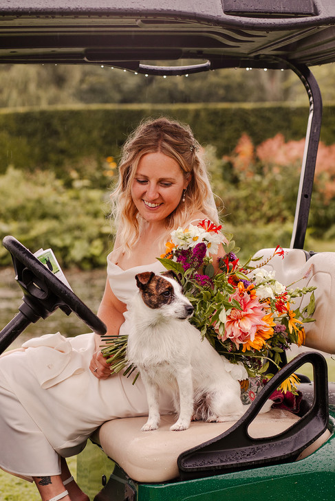 Bride sits in a golf buggy alongside her dog.