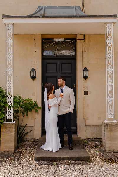 Bride and groom stand close together looking a each other whilst the bride places her hand on his chest, outside Rose Neath House.