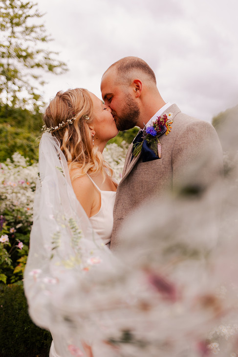 Bride and groom share a kiss with the veil pulled towards the camera