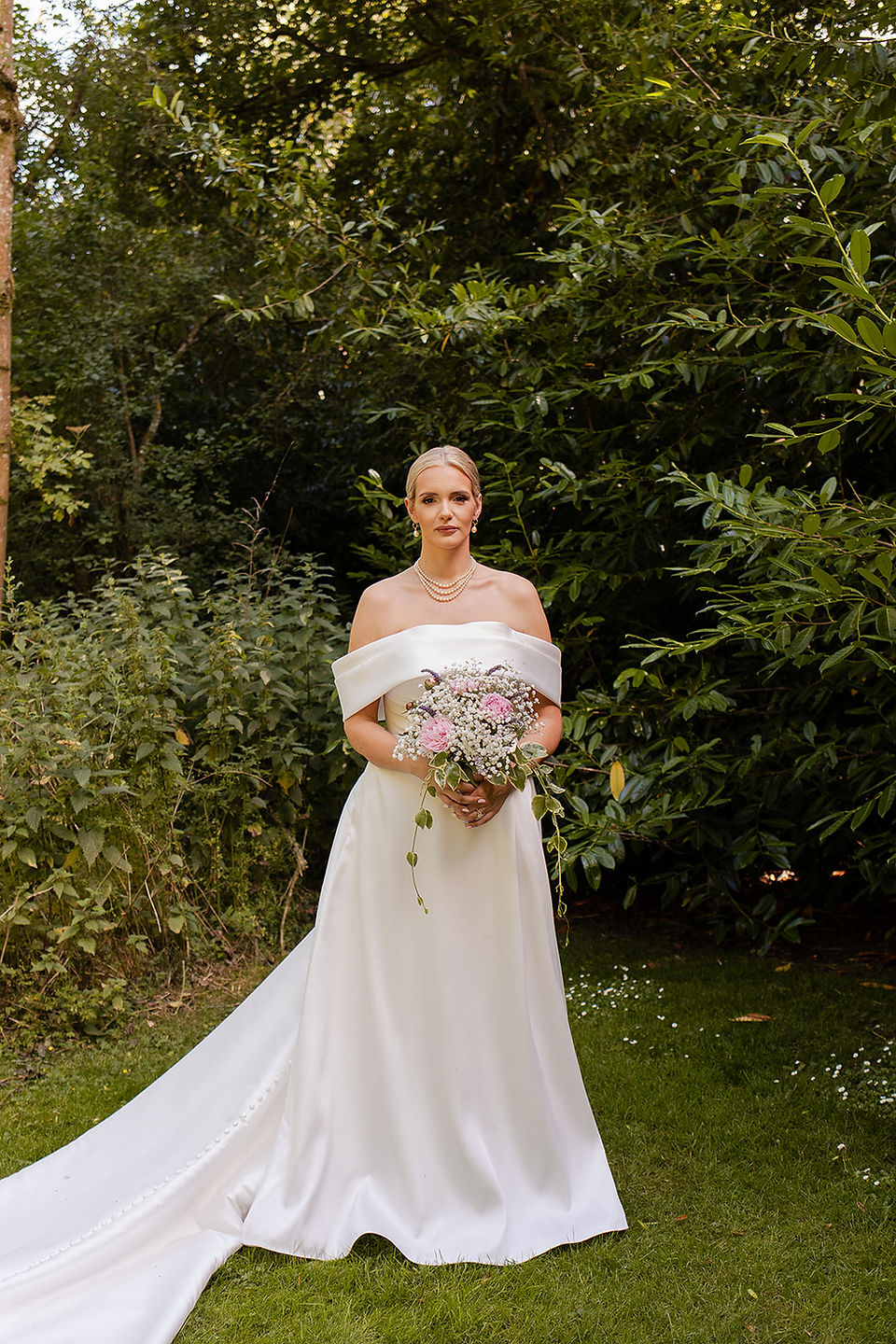 Iona on her own holding her bouquet looking at the camera in the family garden. 