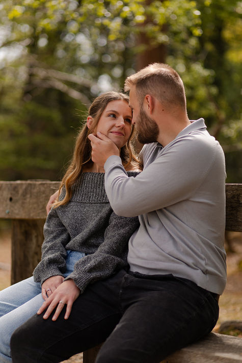 Tom caresses Beth cheek as they sit together on a wooden bench. 