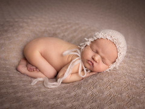 Nyfødt jente sover på magen, tær som perler, jordtoner, hjemmestrikk, lue