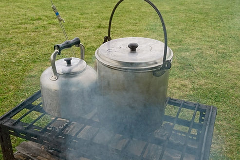 Photo showing altar fire with kettle and pan. Wigwams and tent in the distance